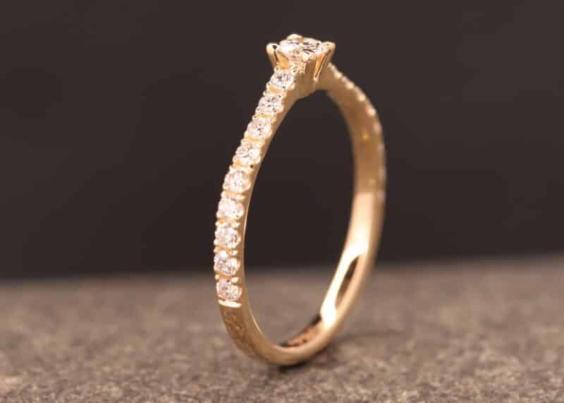 anello di fidanzamento in oro rosa con un grande diamante e piccoli diamanti nella fascia