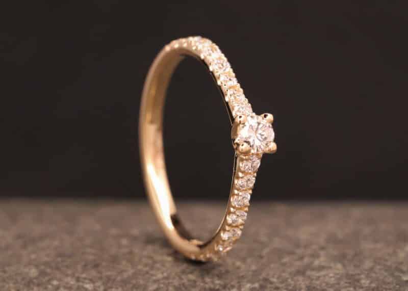 anillo de compromiso en oro rosa con un diamante grande y diamantes pequeños en la banda
